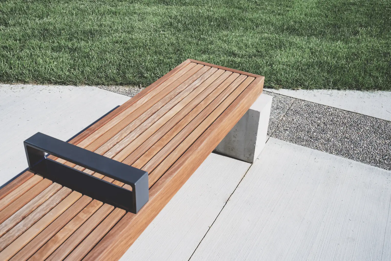 A wooden bench on paving beside a lawn